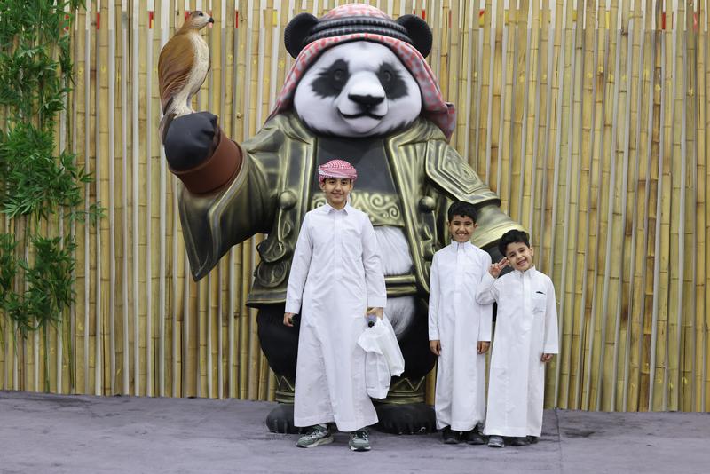 10月6日，在利雅得，沙特儿童在猎鹰节首次设立的中国展区门口的雕塑前合影留念。新华社